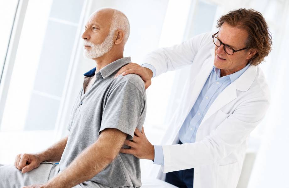 Dr. Knarr steht hinter einem sitzenden Rheumapatienen und behandelt ihn